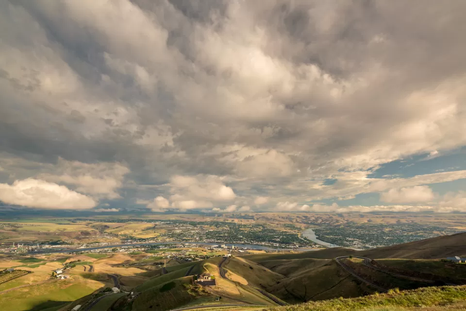 Distant view of Lewiston, Idaho nestled in green hills against cloudy blue sky